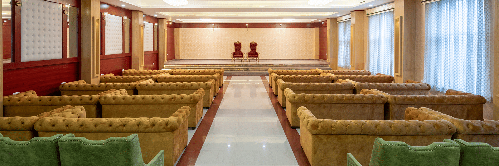 A over the shoulder shot of an expansive banquet hall with brown and green sofas at DLS Tehri Resort and Spa.